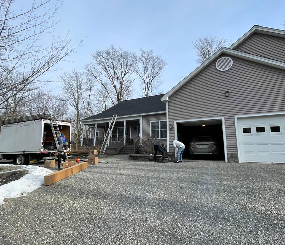 Front of a grey home in Barre Town, VT, with a two-car garage, ladders propped against it, and people preparing to work on the gutters.