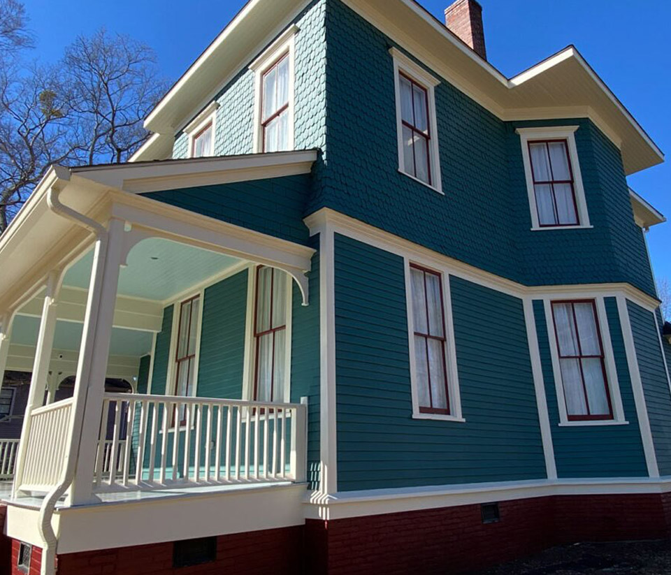 vermont-gutter-company-essex-junction-vt-1 Side of a teal-colored home in Essex Junction, VT with a white porch and newly installed white gutters.