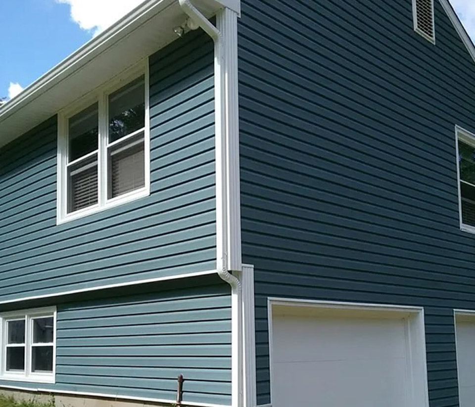 vermont-gutter-company-essex-junction-vt-4 Side exterior of a blue home in Essex Junction, VT showing a newly installed white gutter next to a two-car garage.