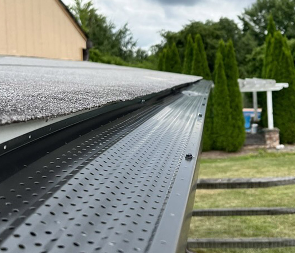 vermont-gutter-company-hartford-vt-6 Close-up of a black gutter with a leaf guard installed on the roof of a home in Hartford, VT.