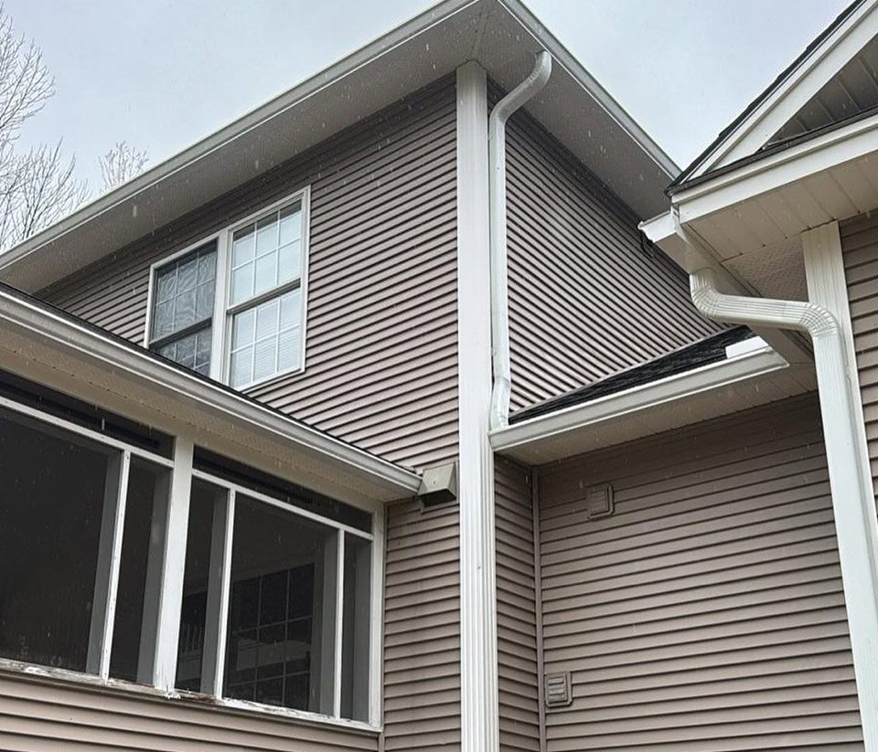 vermont-gutter-company-middlebury-vt-4 The side of a tan colored home in Middlebury, VT with a gutter running along the side of the home.