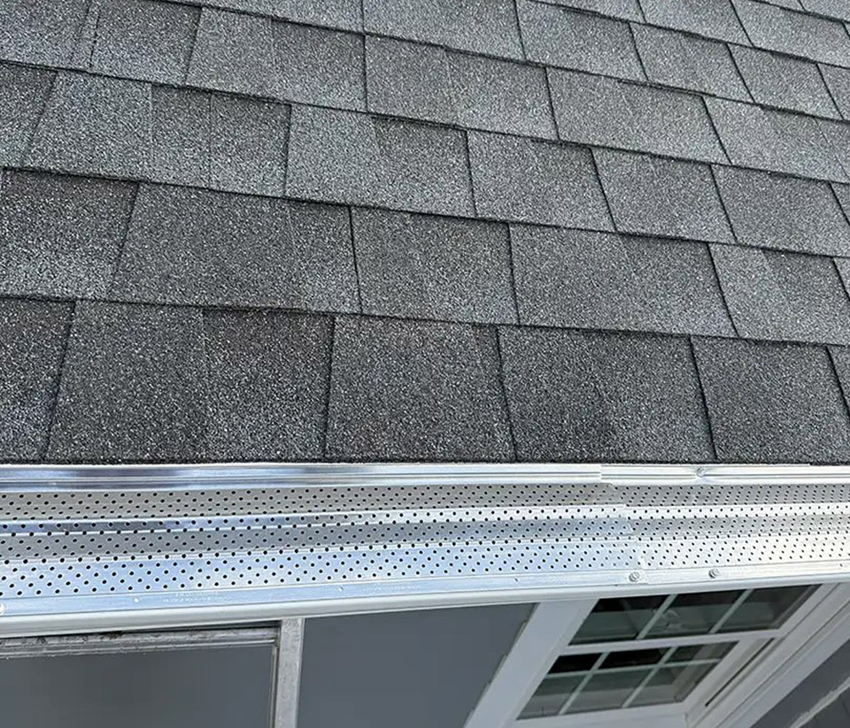 vermont-gutter-company-middlebury-vt-6 Close-up of a shingle roof in Middlebury, VT, showing gutters with attached gutter guards.