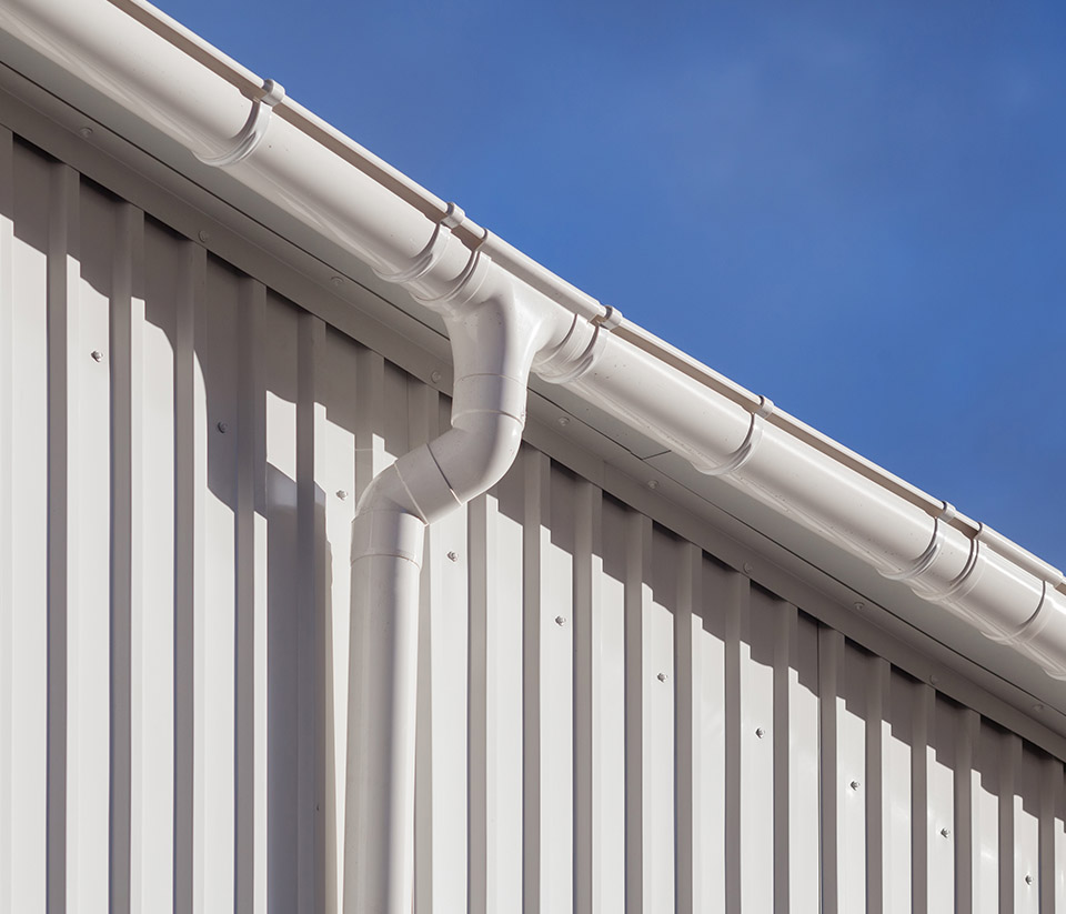 vermont-gutter-company-milton-vt-7 Close-up of the side of a white metal commercial building with white gutters installed along the edge in Milton, VT.