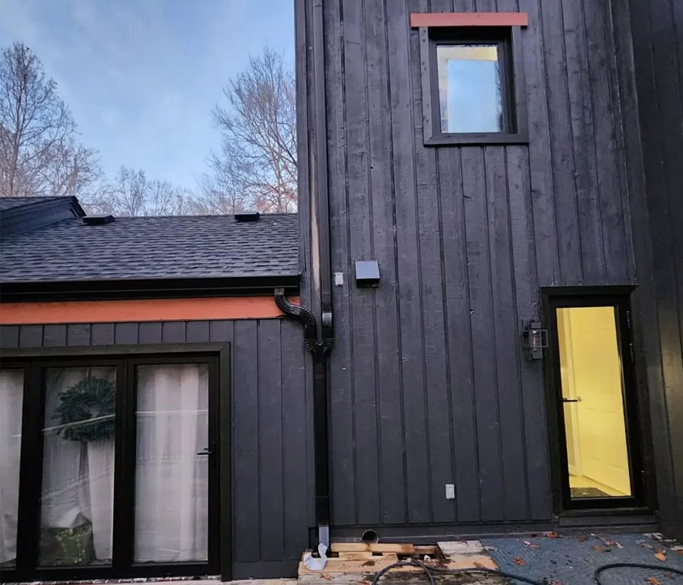 vermont-gutter-company-shelburne-vt-1 The side of a black home in Shelburne, VT, featuring a yellow door, tall windows, and newly installed gutters.