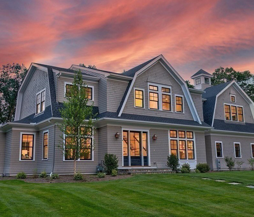 vermont-gutter-company-south-burlington-vt-2 Exterior of a tan home in South Burlington, VT, with multiple windows, green grass, a sunset sky, and newly installed gutters.