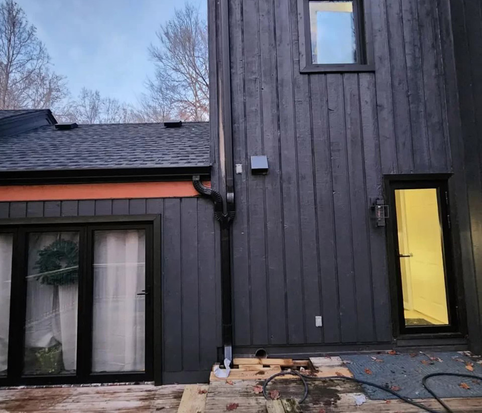 vermont-gutter-company-st-albans-vt-1 The side view of a black home with a yellow door and tall windows in St. Albans, VT.