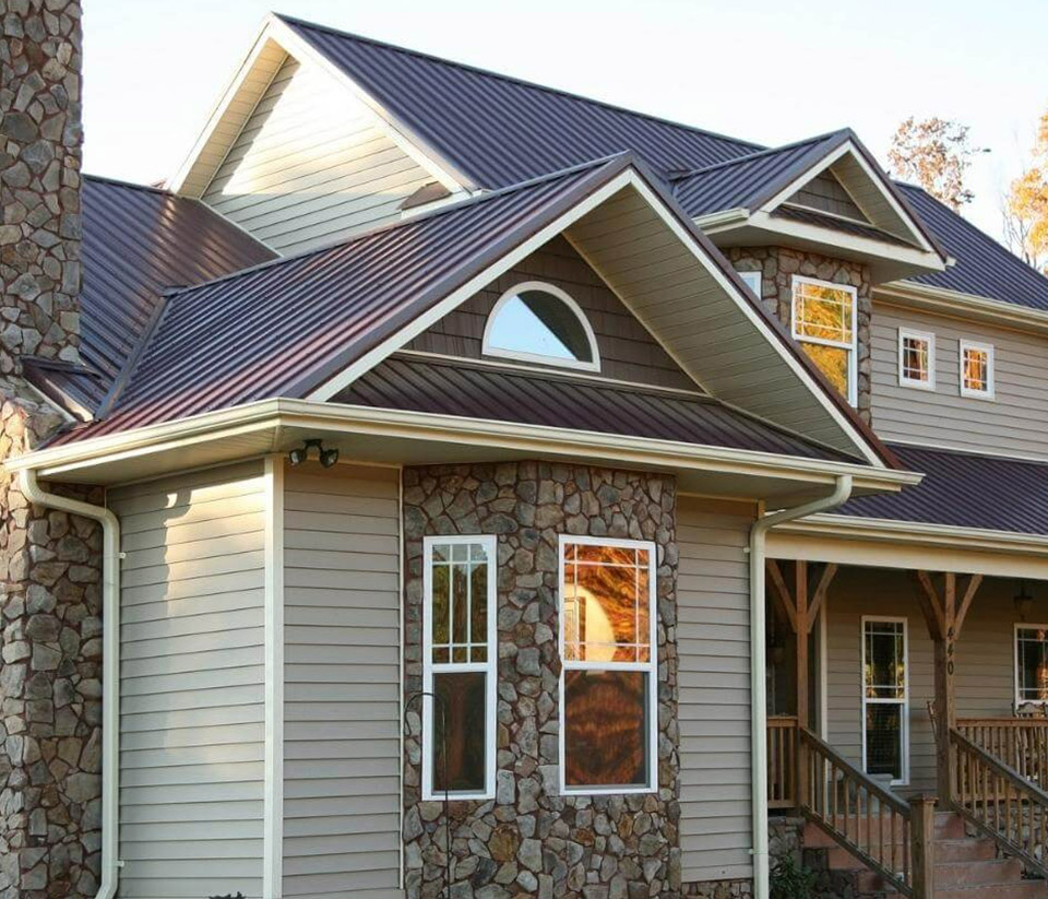 vermont-gutter-company-st-albans-vt-3 A home in St. Albans, VT, with siding, a wooden porch, stone detailing around tall windows, and newly installed white gutters.