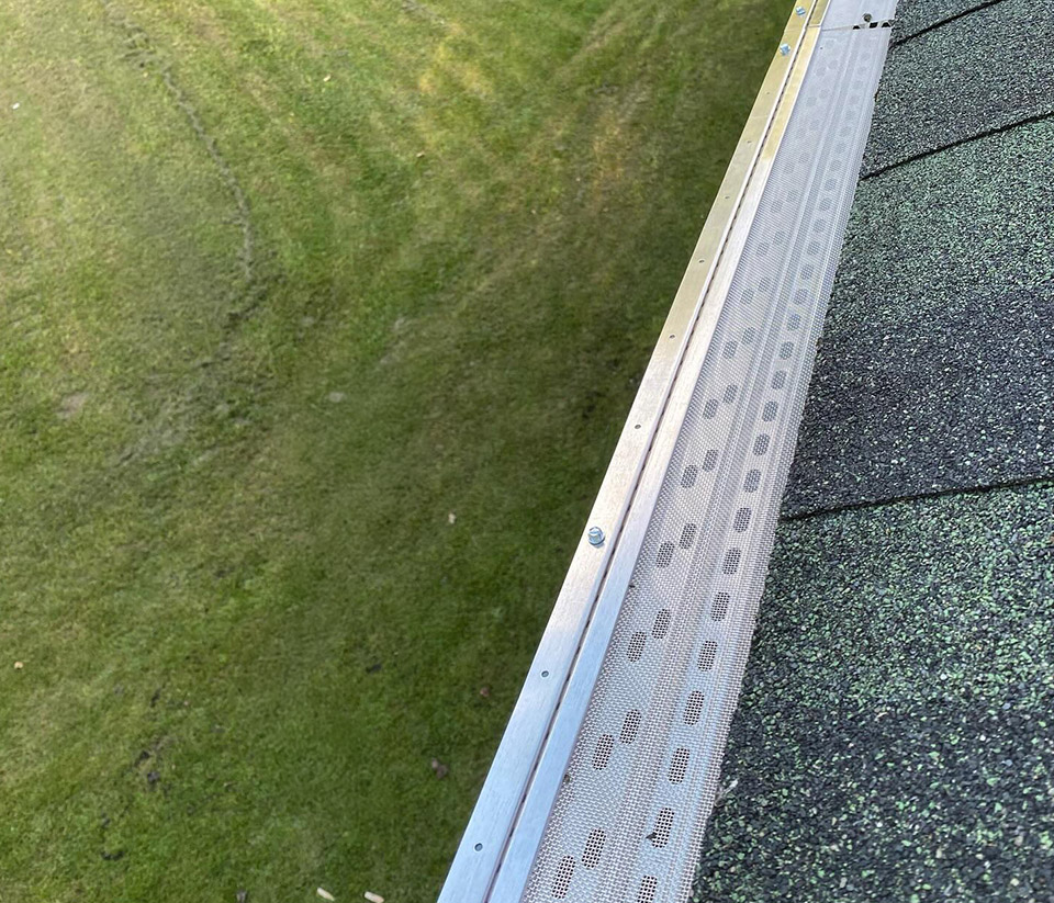 vermont-gutter-company-st-albans-vt-6 A close-up of a white gutter recently installed on the roof of a home in St. Albans, VT against the view of green grass in the background.