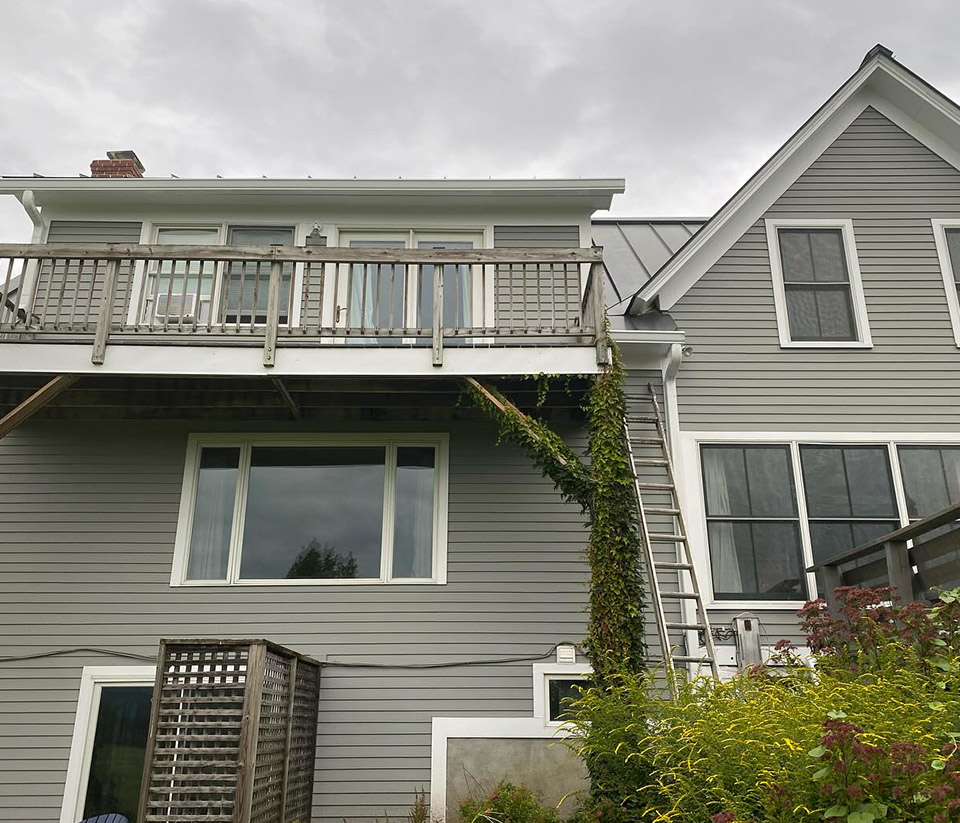 vermont-gutter-company-waterbury-vt-4 Home in Waterbury, VT, with a second-level deck and a ladder propped against it as someone prepares to work on the gutters.