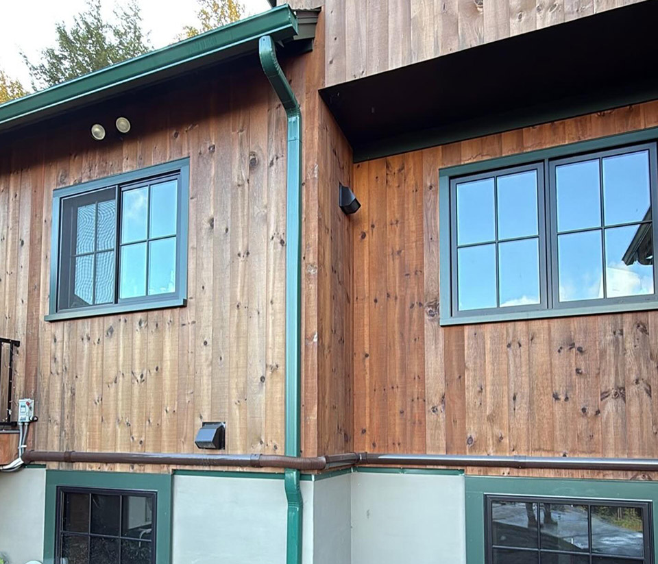 vermont-gutter-company-waterbury-vt-5 Home in Waterbury, VT, with natural wood siding, windows with dark green trim, and green gutters.